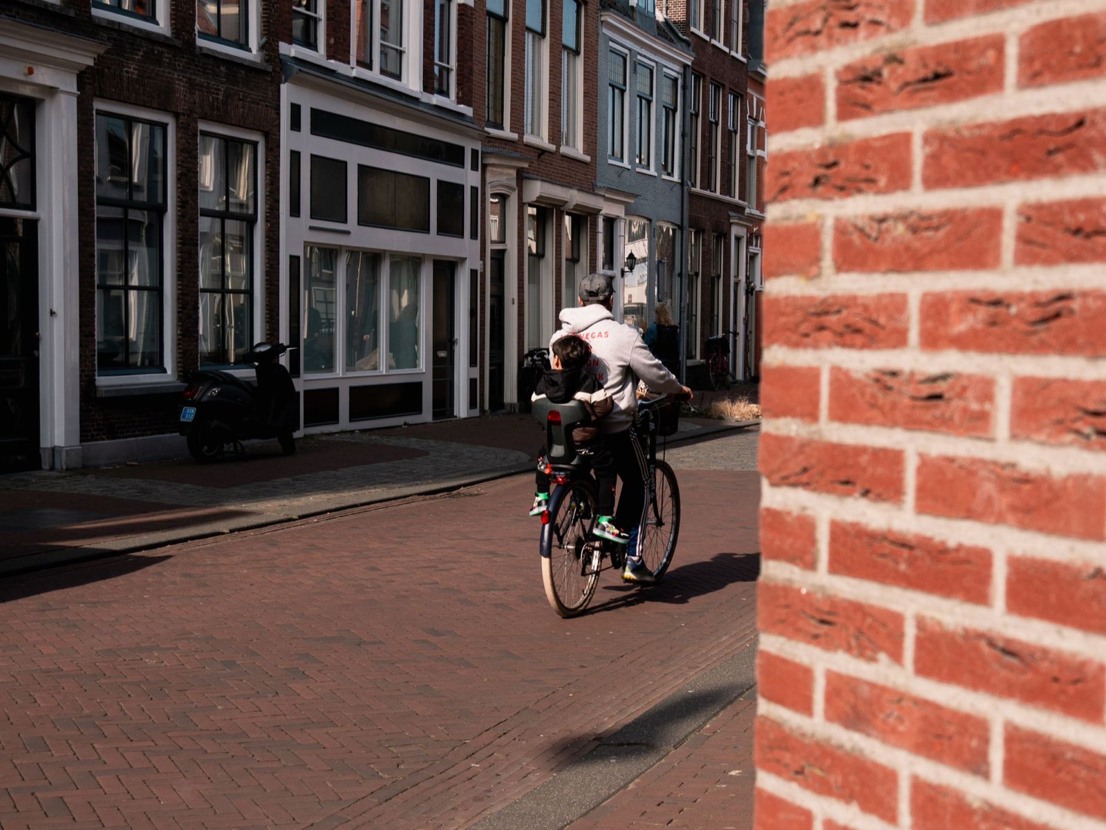 Volwassene fietst met kind achterop over klinkers in een Haarlemse straat
