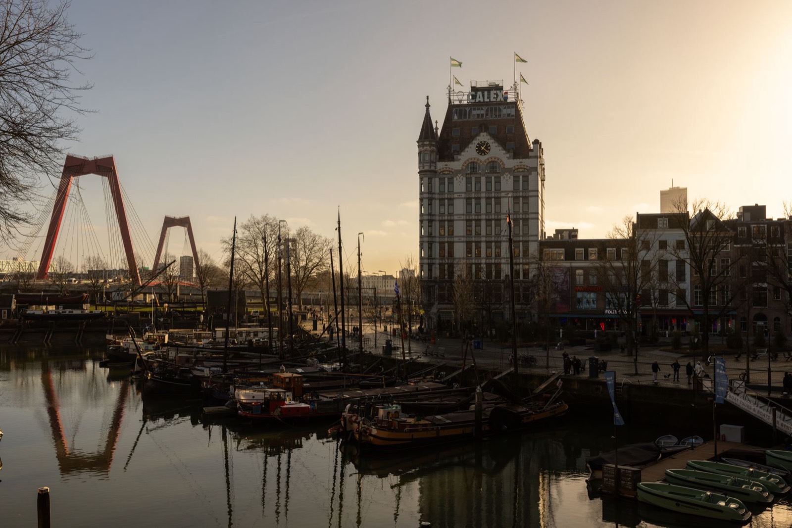 Havenkade in warm licht met zeilschepen en een rode tuibrug